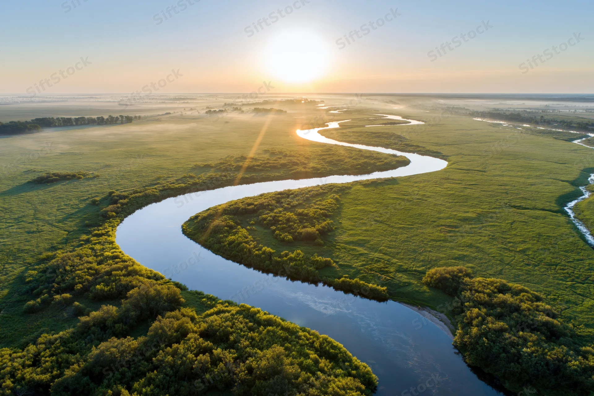 Aerial view of a winding river snaking through flat green wetlands at sunrise