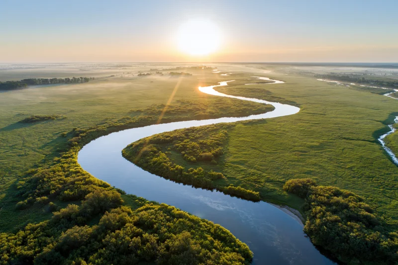 Aerial view of a winding river snaking through flat green wetlands at sunrise