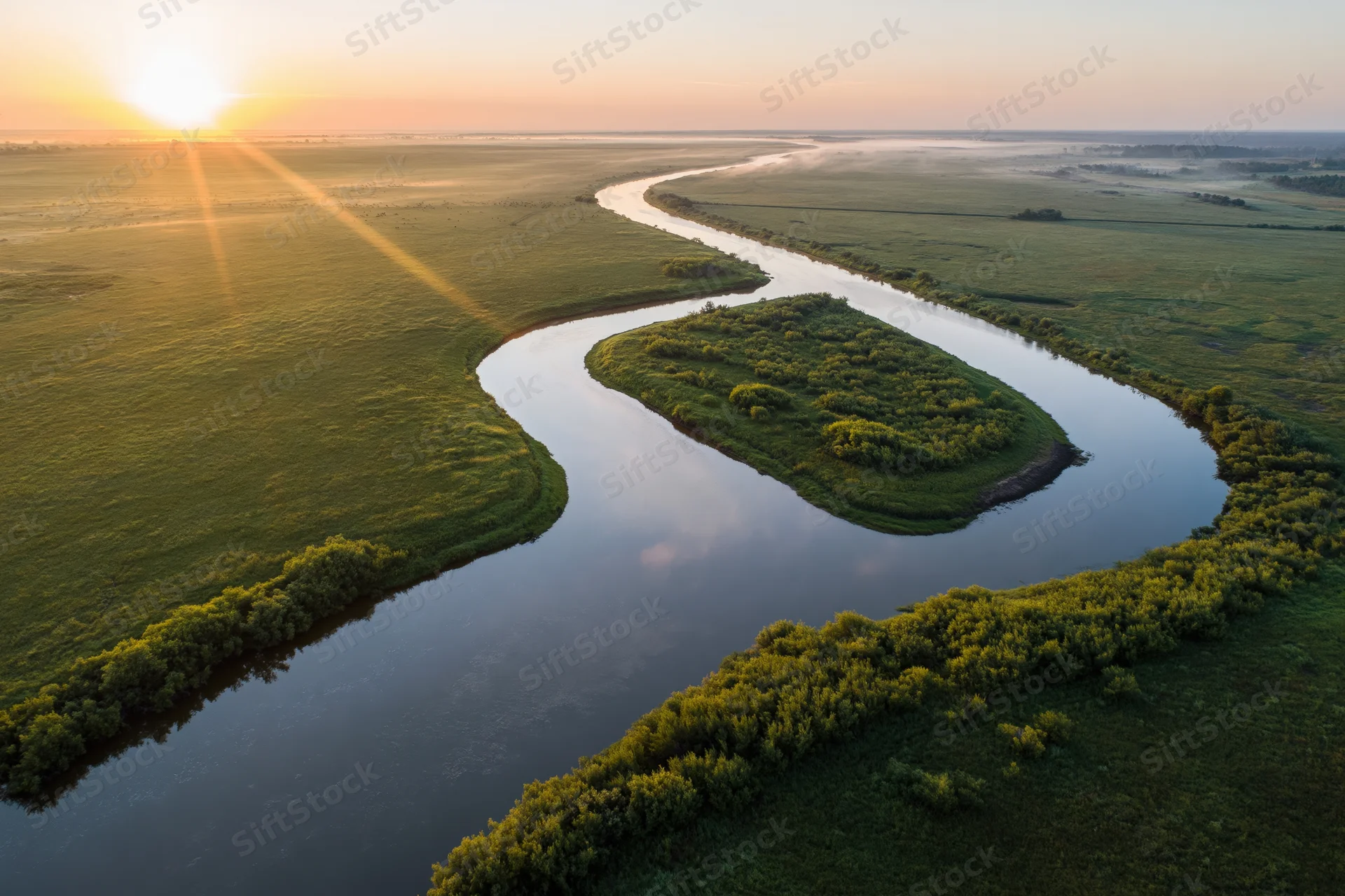 Aerial view of a winding river meandering through flat green wetlands at sunrise