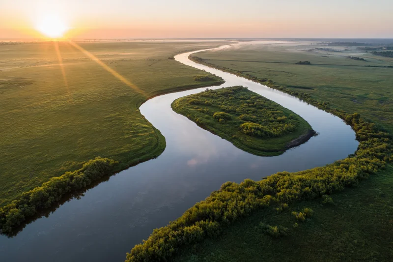 Aerial view of a winding river meandering through flat green wetlands at sunrise