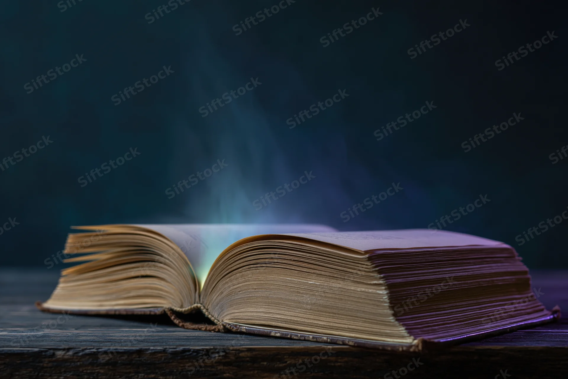Open old book glowing with light and smoke on dark wooden table
