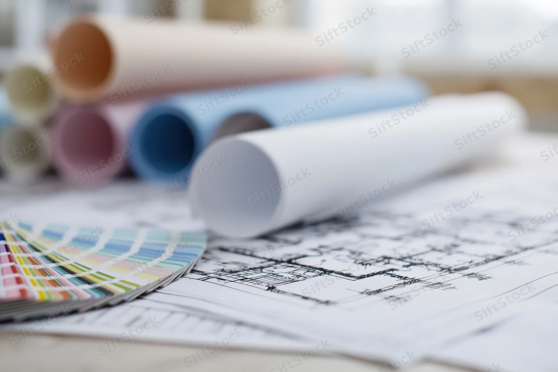 Architectural blueprints spread on a desk with color swatch and rolled plans