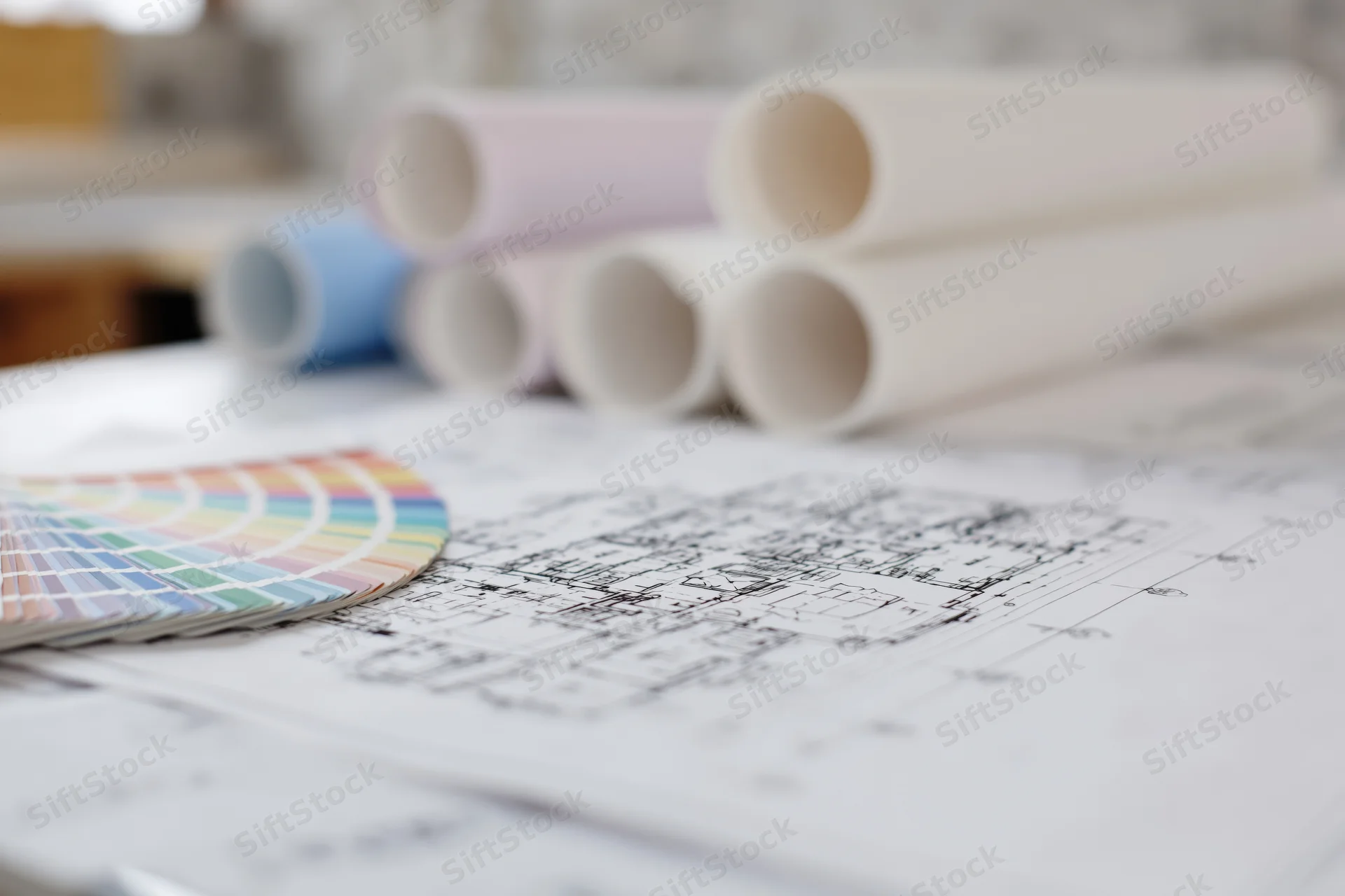 Architectural blueprints spread on a table with rolled plans and a color swatch nearby