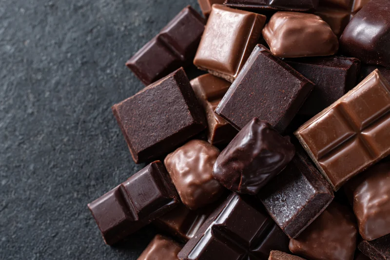 Assorted chocolate bars and praline candies piled on dark surface, close-up overhead view