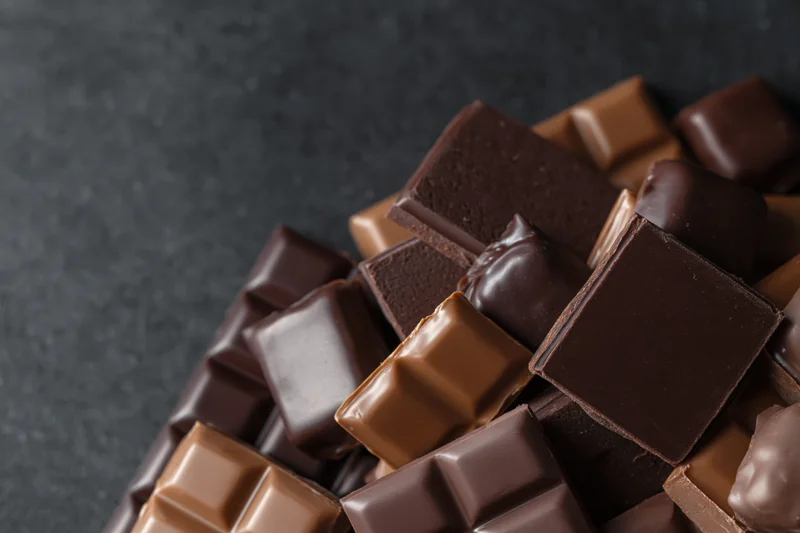 Assorted chocolate bars and praline candies piled on a dark surface with copyspace on the left