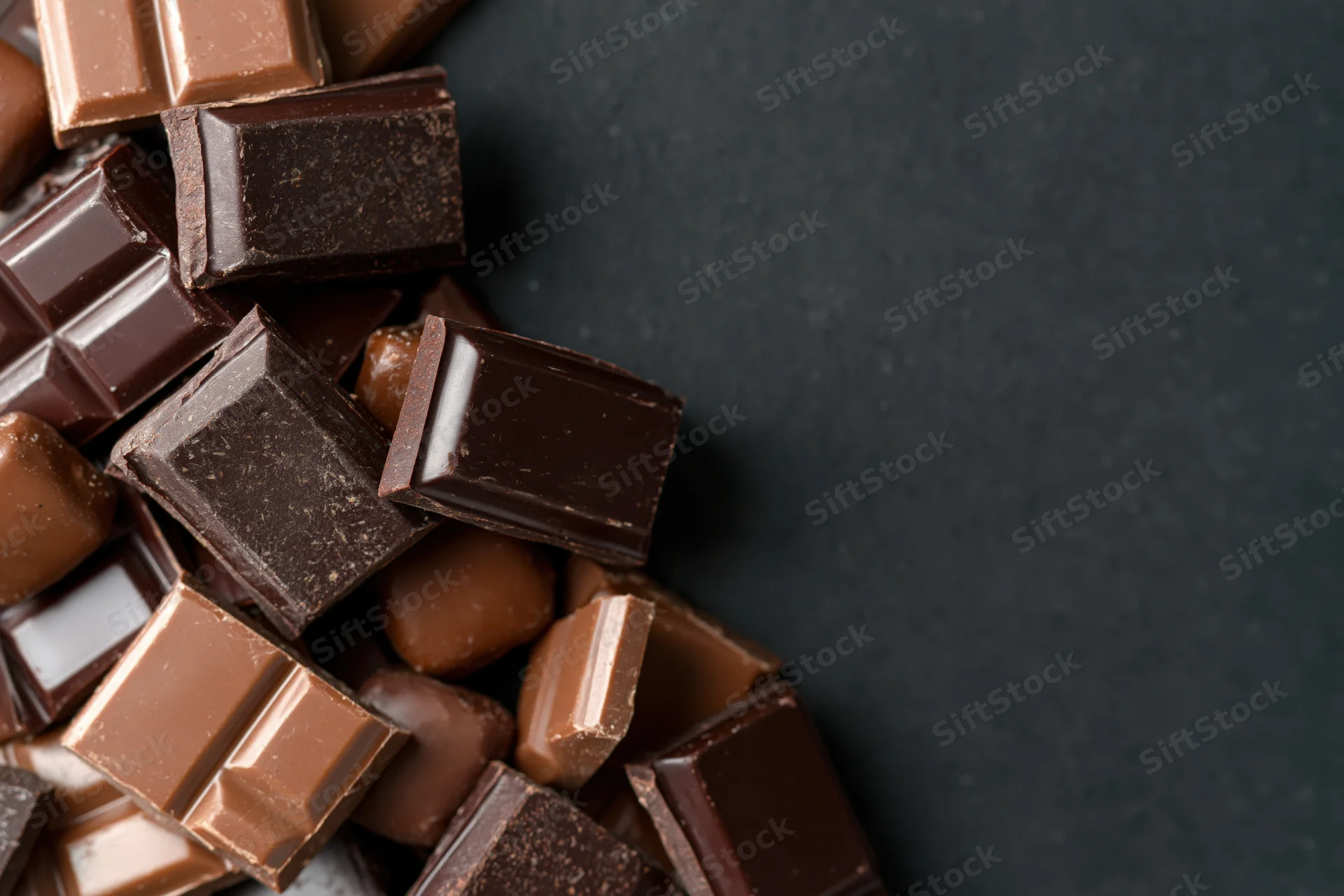 Assorted chocolate bars and praline candies scattered in a corner on dark surface with copyspace