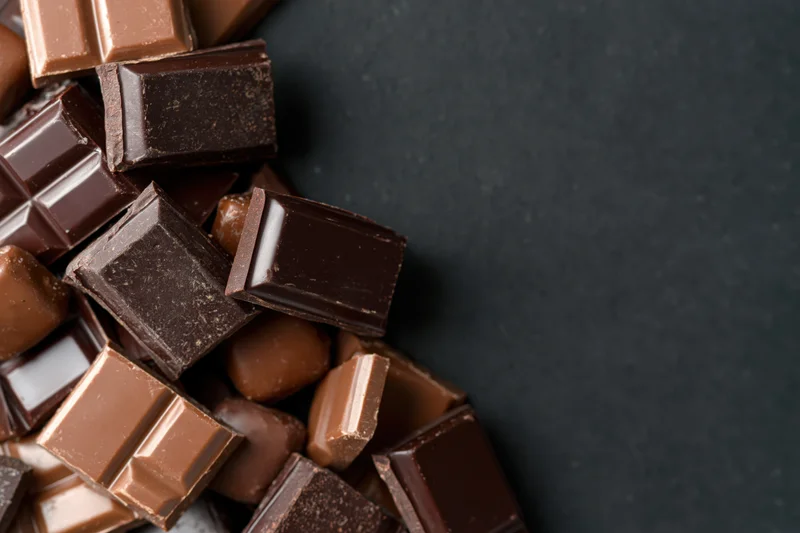 Assorted chocolate bars and praline candies scattered in a corner on dark surface with copyspace