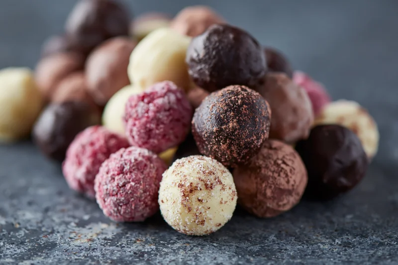 Assorted handmade chocolate truffles and pralines piled loose on a dark stone surface
