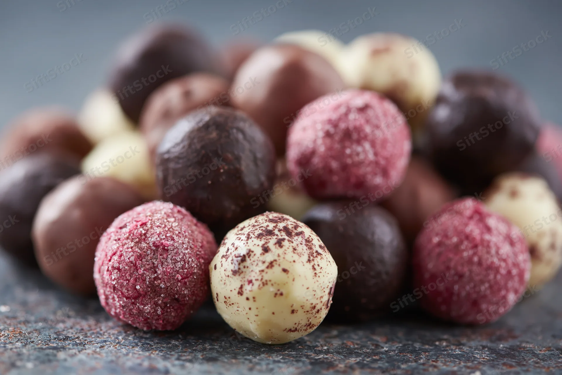 Assorted handmade chocolate truffles and pralines piled loose on a dark stone surface