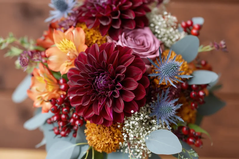 Autumn wedding bouquet with burgundy dahlias, orange alstroemeria, and red berries arranged with eucalyptus and thistle