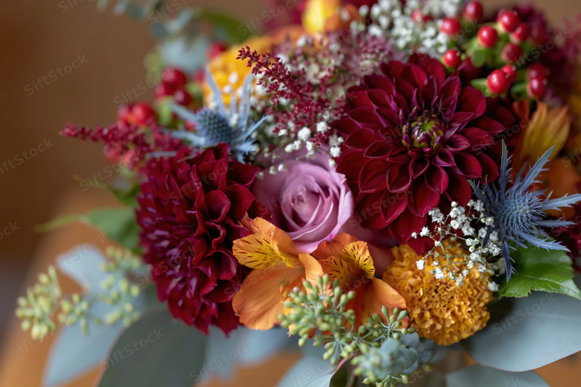 Autumn wedding bouquet with burgundy dahlias, pink roses, orange alstroemeria, blue thistle, and green eucalyptus foliage