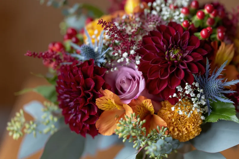 Autumn wedding bouquet with burgundy dahlias, pink roses, orange alstroemeria, blue thistle, and green eucalyptus foliage