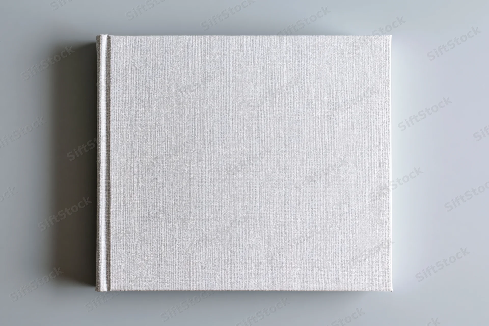 Blank white hardcover book lying flat centered on gray surface