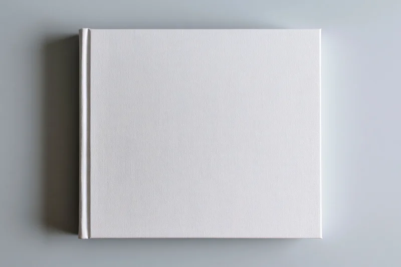 Blank white hardcover book lying flat centered on gray surface