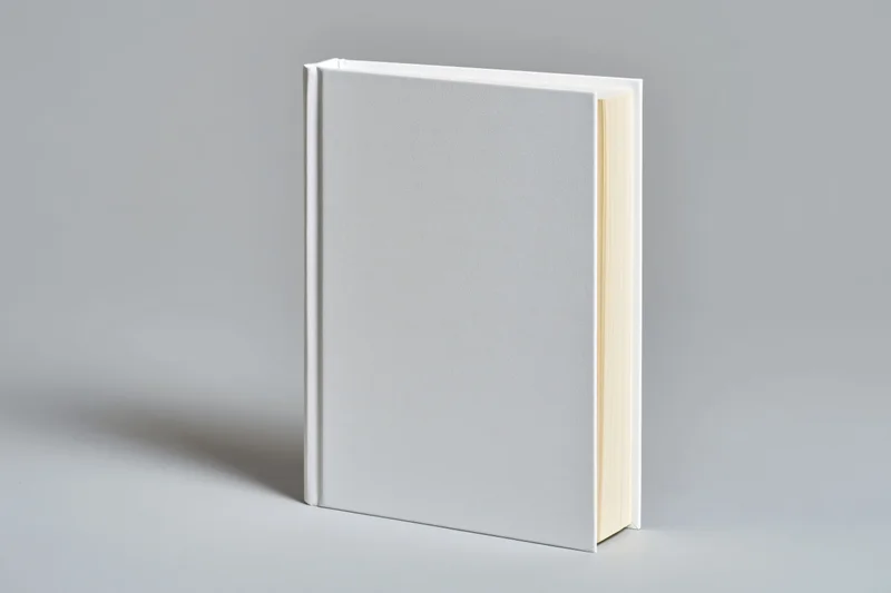 Blank white hardcover book upright on a light grey surface