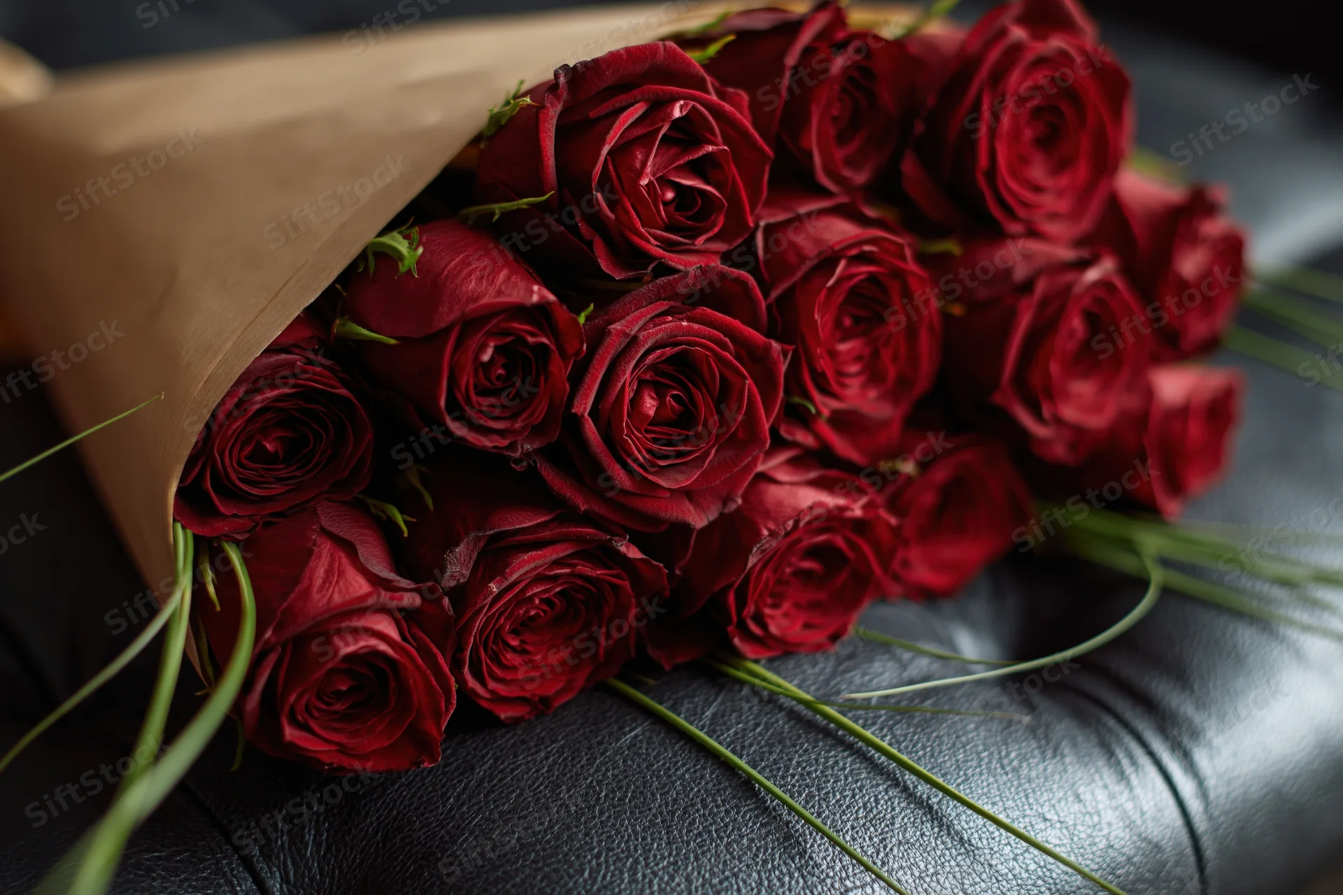 Bouquet of deep red roses wrapped in kraft paper cone resting on dark leather couch