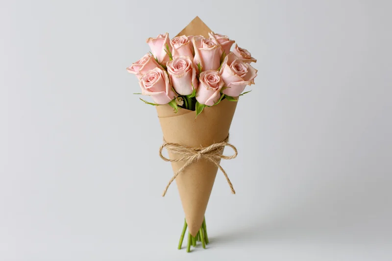 Bouquet of soft pink roses wrapped in kraft paper cone tied with twine on white background