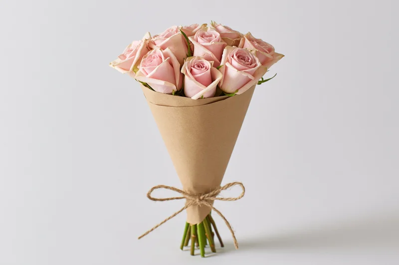 Bouquet of soft pink roses wrapped in kraft paper cone tied with twine on white background