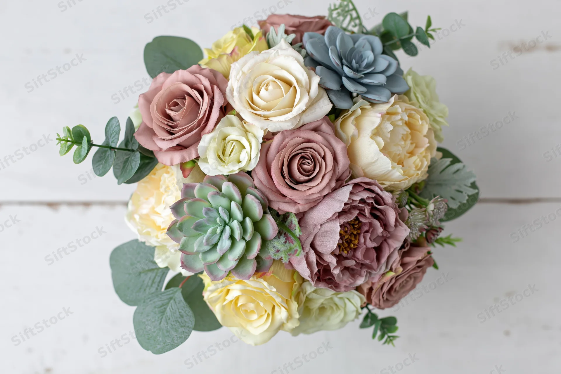 Overhead view of a bridal bouquet with roses, succulents and eucalyptus on a white wooden surface