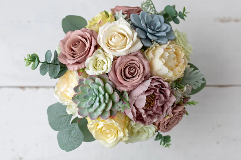 Overhead view of a bridal bouquet with roses, succulents and eucalyptus on a white wooden surface