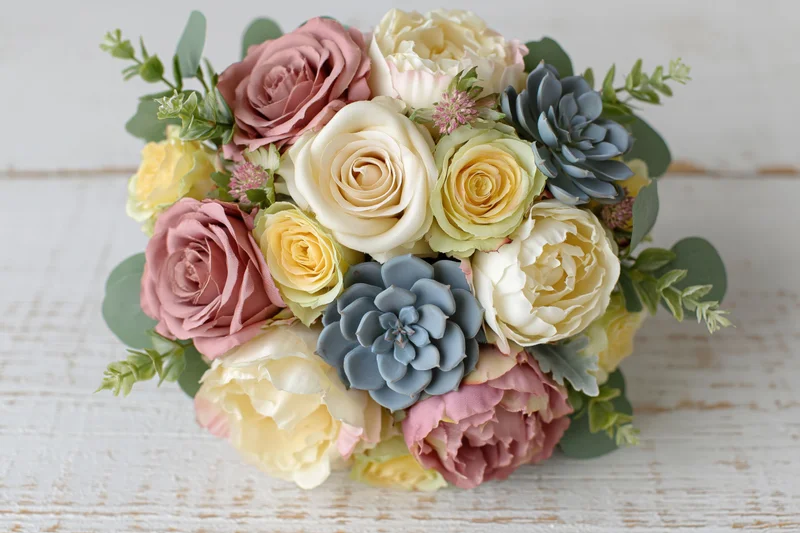 Bridal bouquet with roses and succulents arranged on a white wooden surface viewed from above