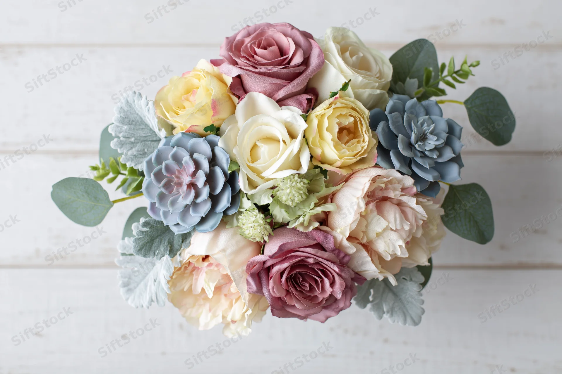 Overhead view of a pastel-colored bridal bouquet with roses, peonies, succulents and eucalyptus on a white wooden surface