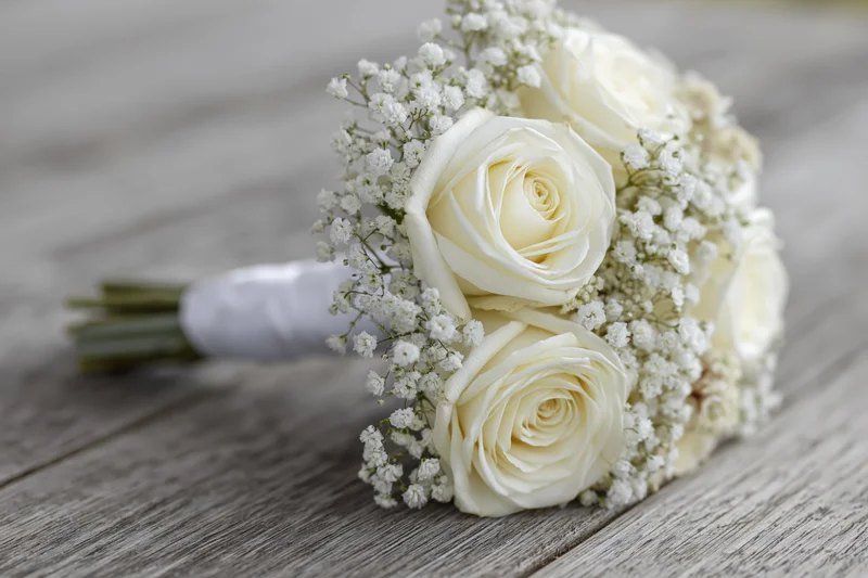 Bridal bouquet of white roses and baby's breath resting on a wooden surface