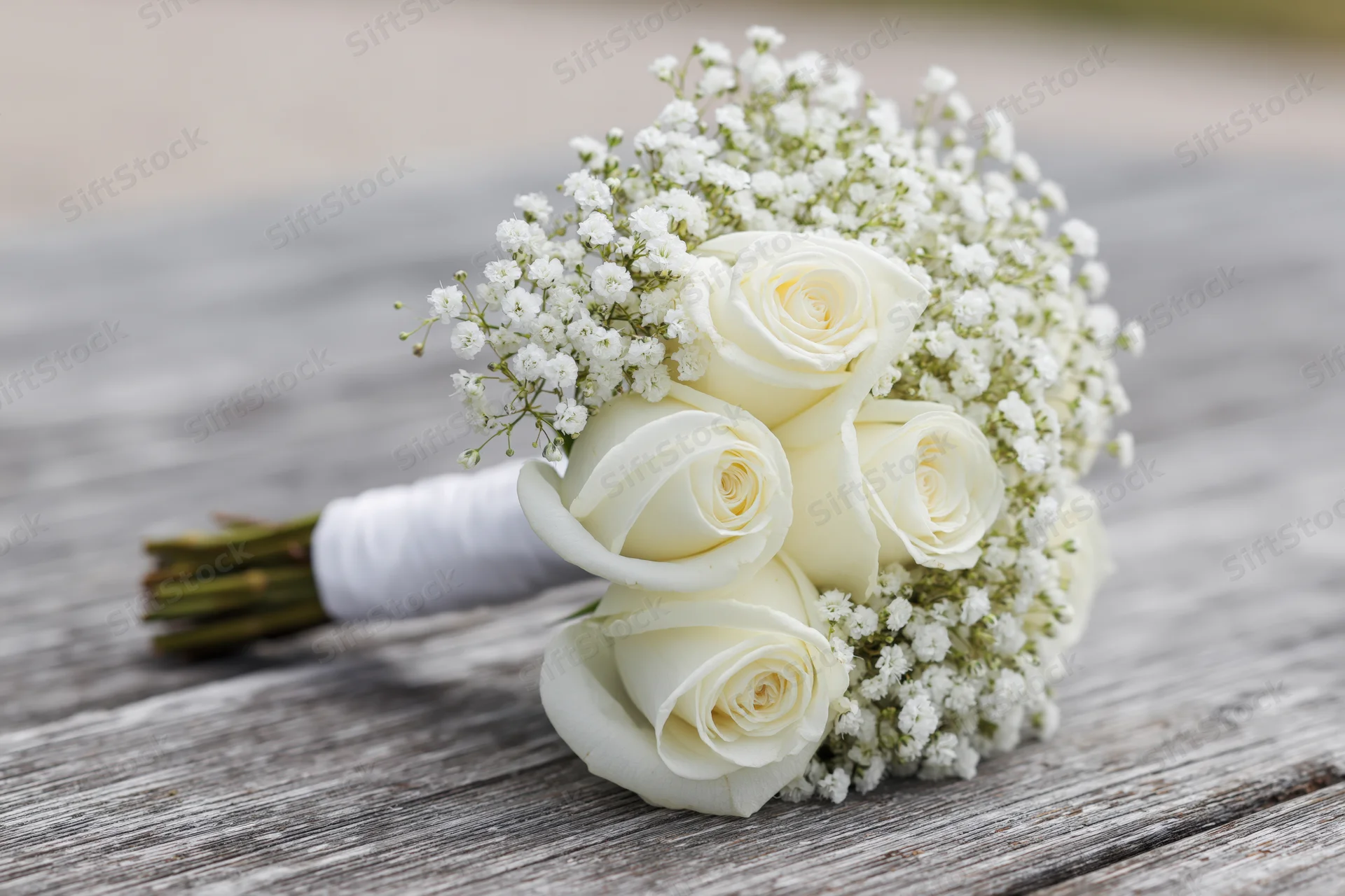 Bridal bouquet of white roses and baby's breath resting on a weathered wooden surface