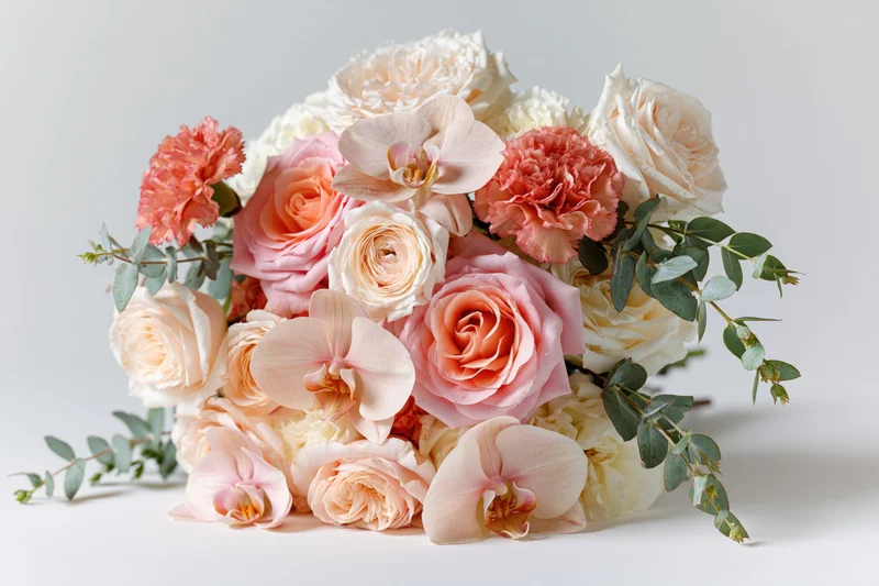 Bridal bouquet of pink and cream roses, orchids, and carnations with eucalyptus on white surface