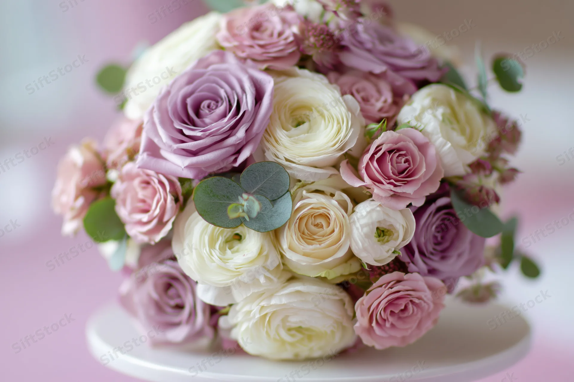 Bridal bouquet of pink, white and lavender roses with eucalyptus on a white cake stand