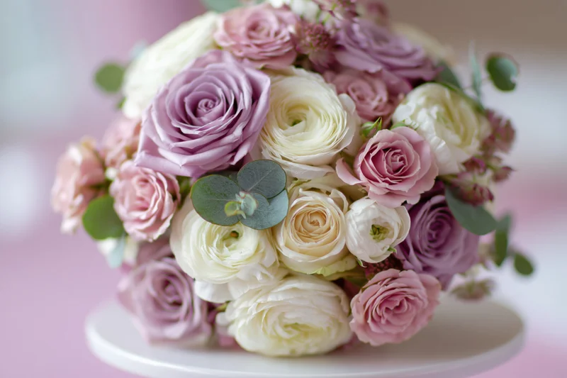 Bridal bouquet of pink, white and lavender roses with eucalyptus on a white cake stand