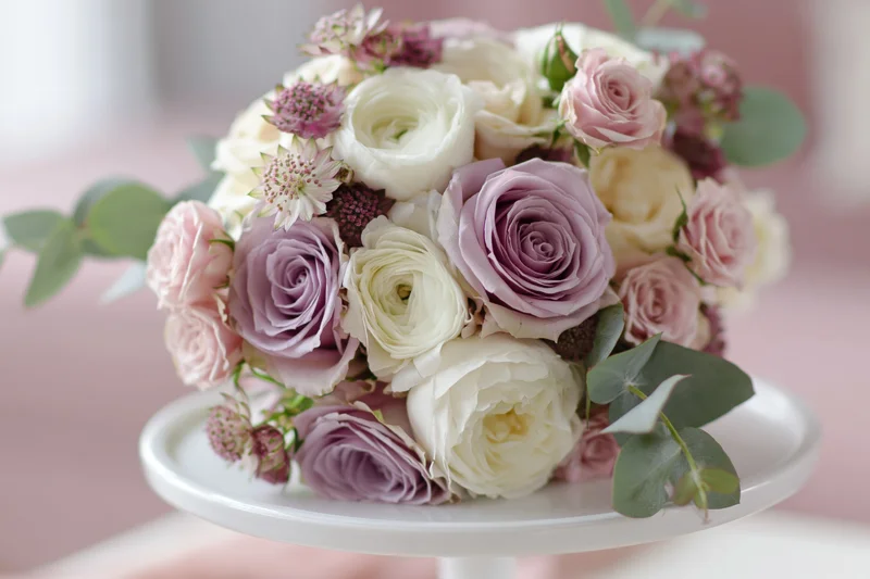 Bridal bouquet of white, pink and lavender roses with eucalyptus greenery resting on a white cake stand
