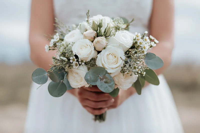 Bride holding a white and green floral bouquet at waist height outdoors