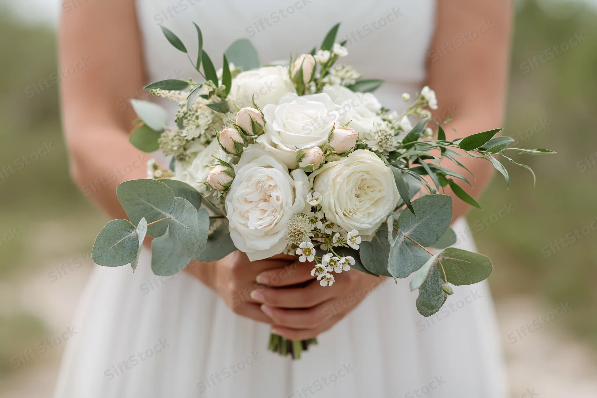 Bride holding a white and green floral bouquet at waist height outdoors