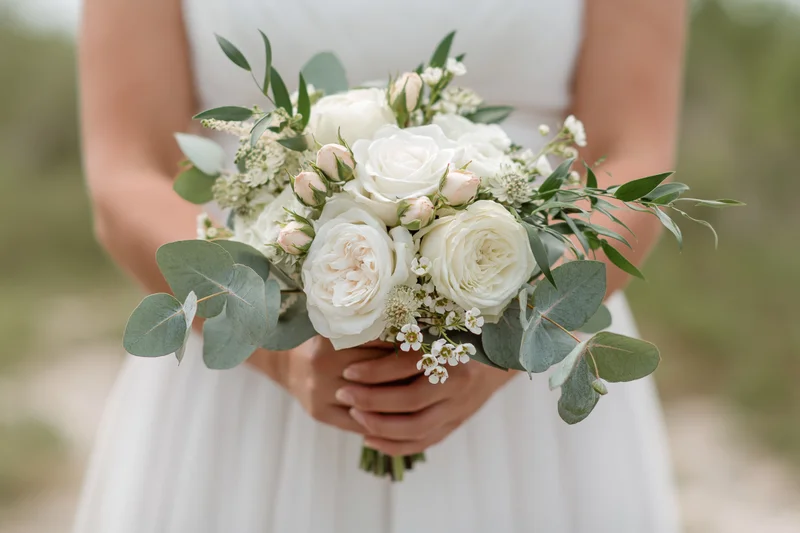 Bride holding a white and green floral bouquet at waist height outdoors