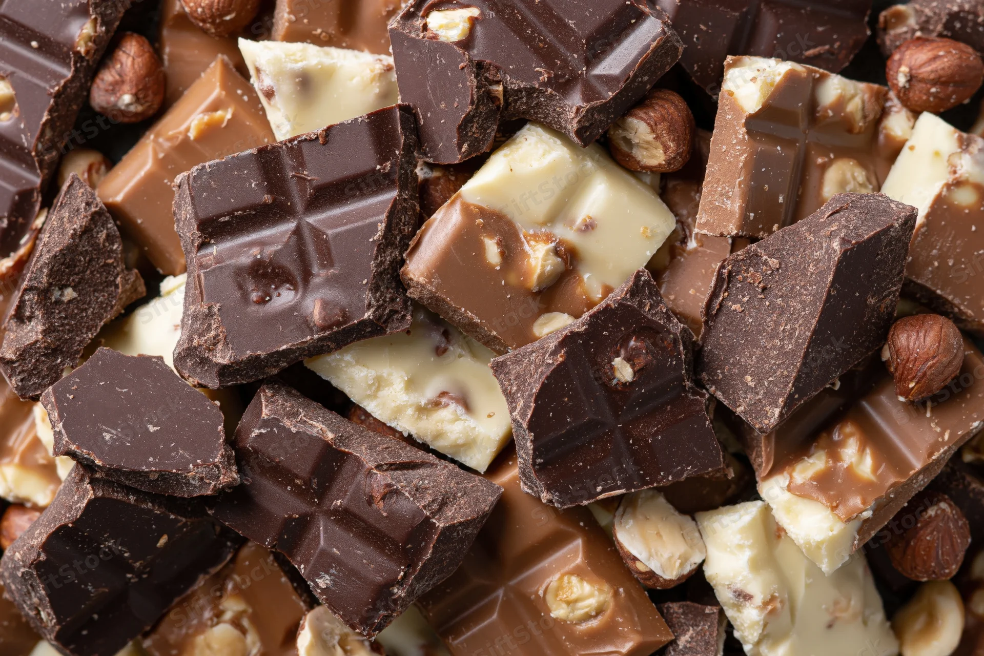 Broken chocolate pieces with hazelnuts piled together in a closeup view