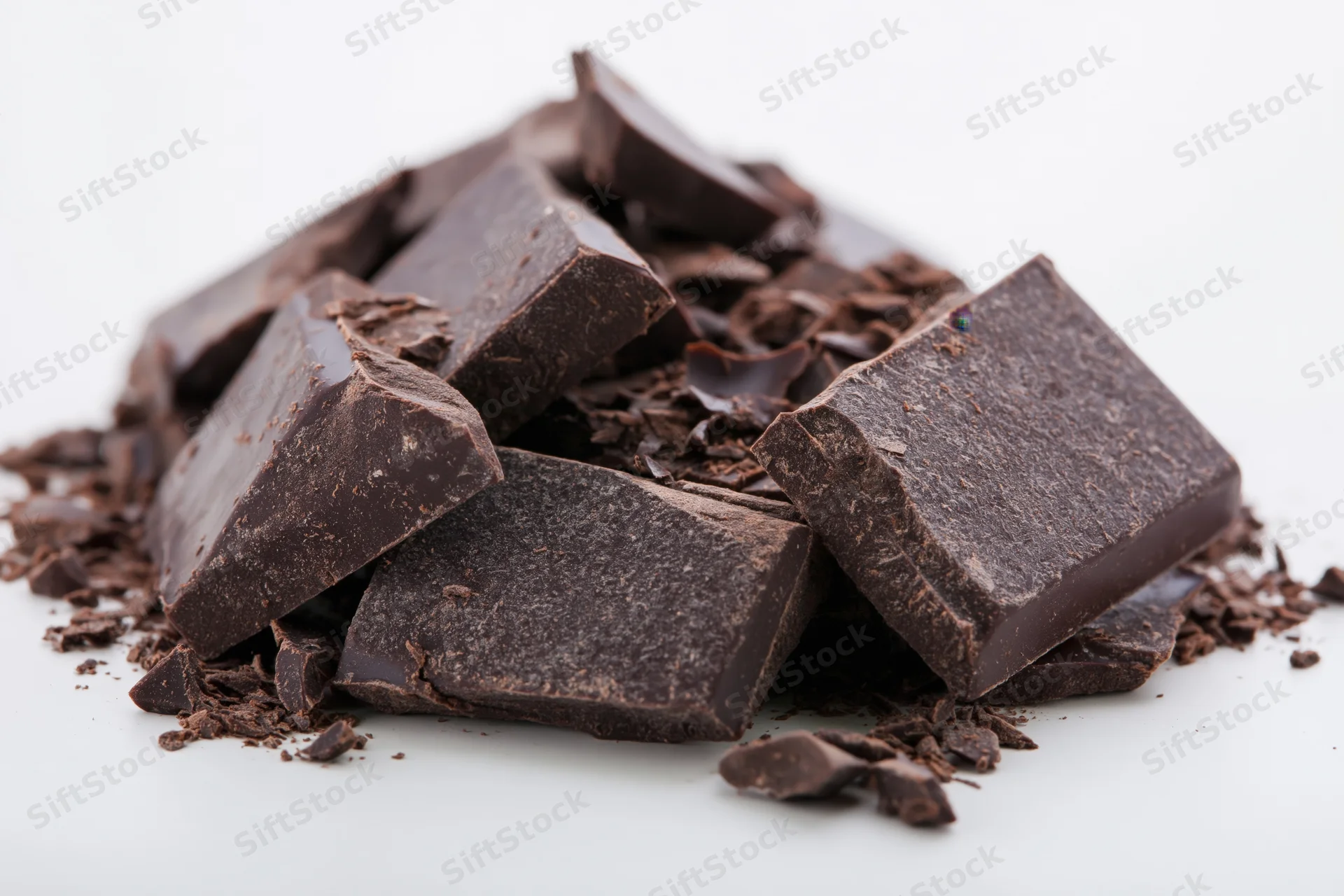 Broken dark chocolate chunks piled together on white background