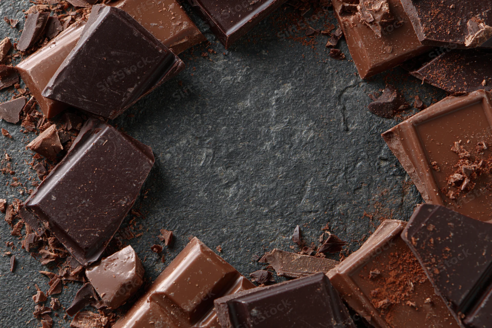 Broken dark and milk chocolate pieces arranged loosely around a slate surface