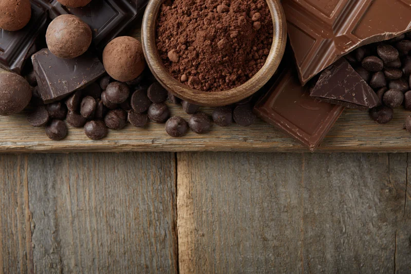Broken dark and milk chocolate bars with cocoa powder and truffles on a wooden surface
