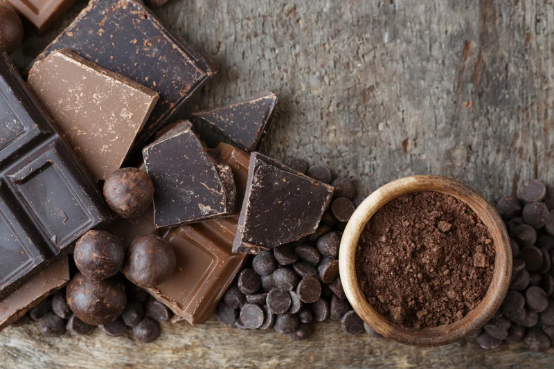 Broken dark and milk chocolate bars with cocoa powder in a wooden bowl on rustic wood surface