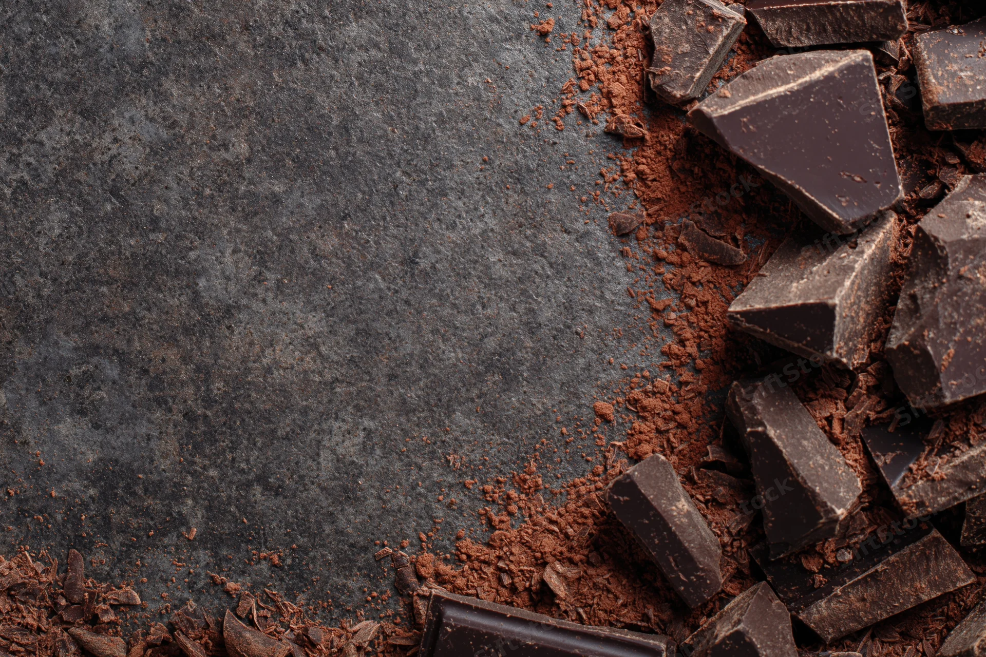 Broken dark chocolate chunks and cocoa shavings scattered on a gray stone surface