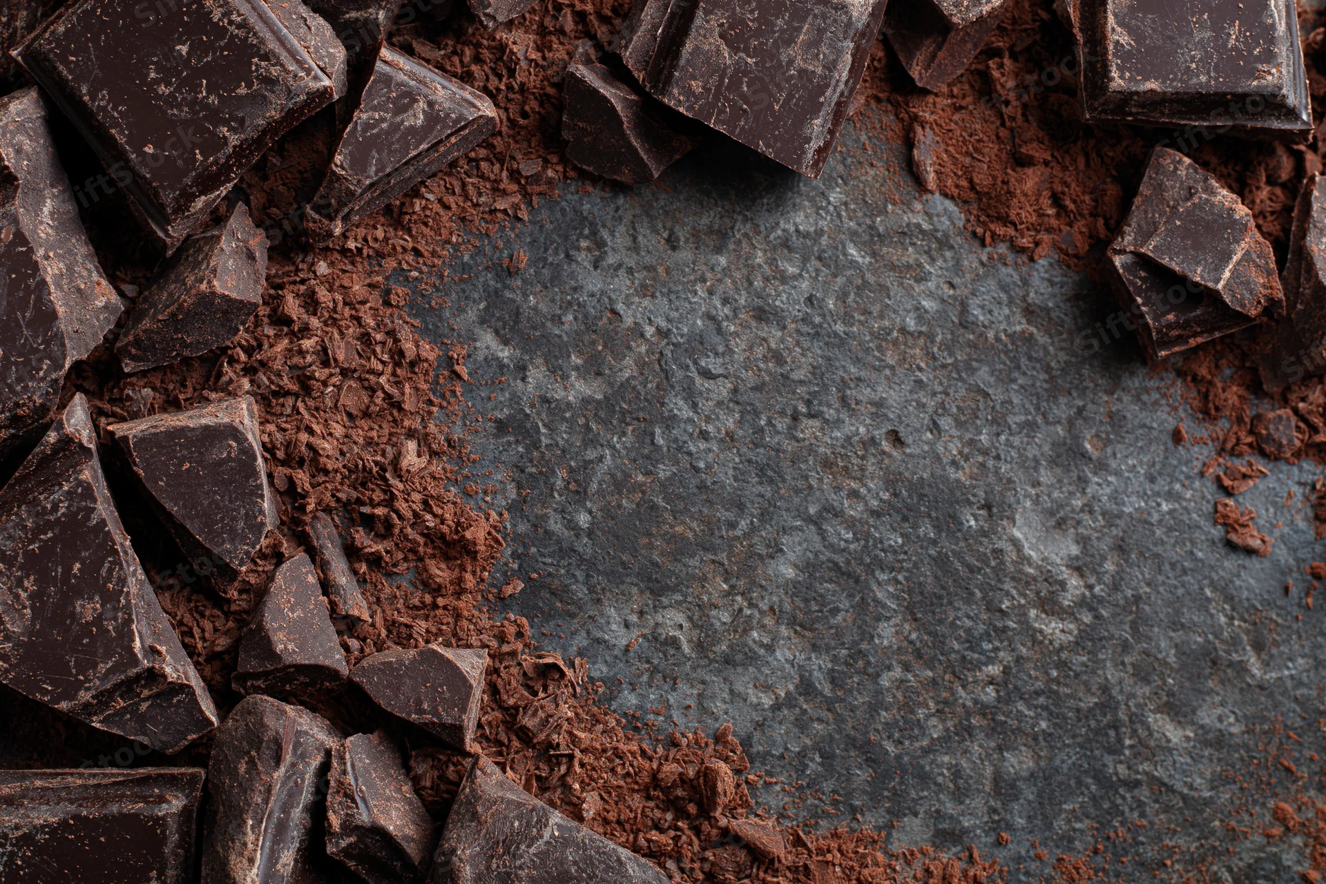 Broken dark chocolate chunks and cocoa shavings arranged in a circular border on a slate surface with central copyspace