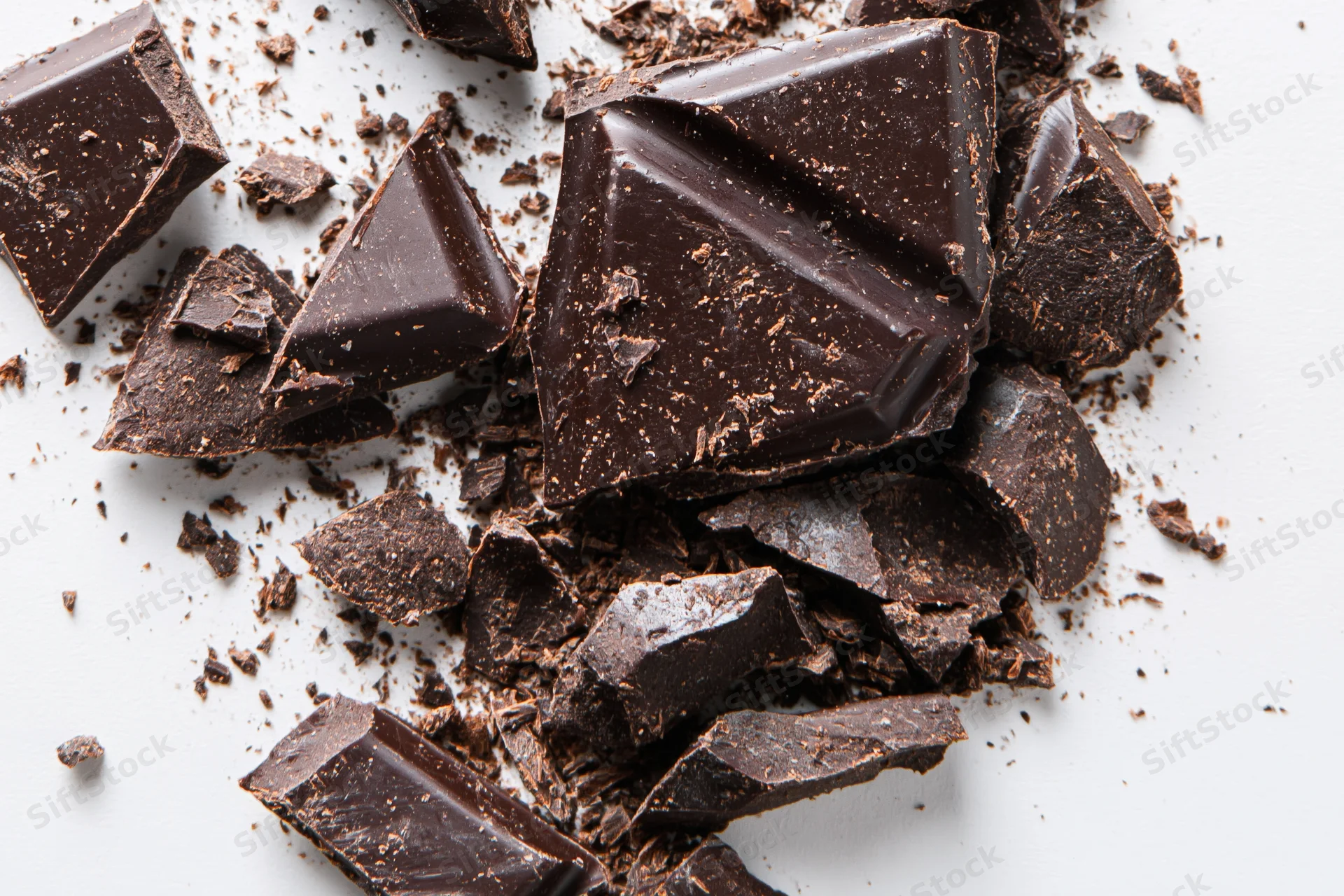 Broken dark chocolate pieces and crumbs scattered across a white surface