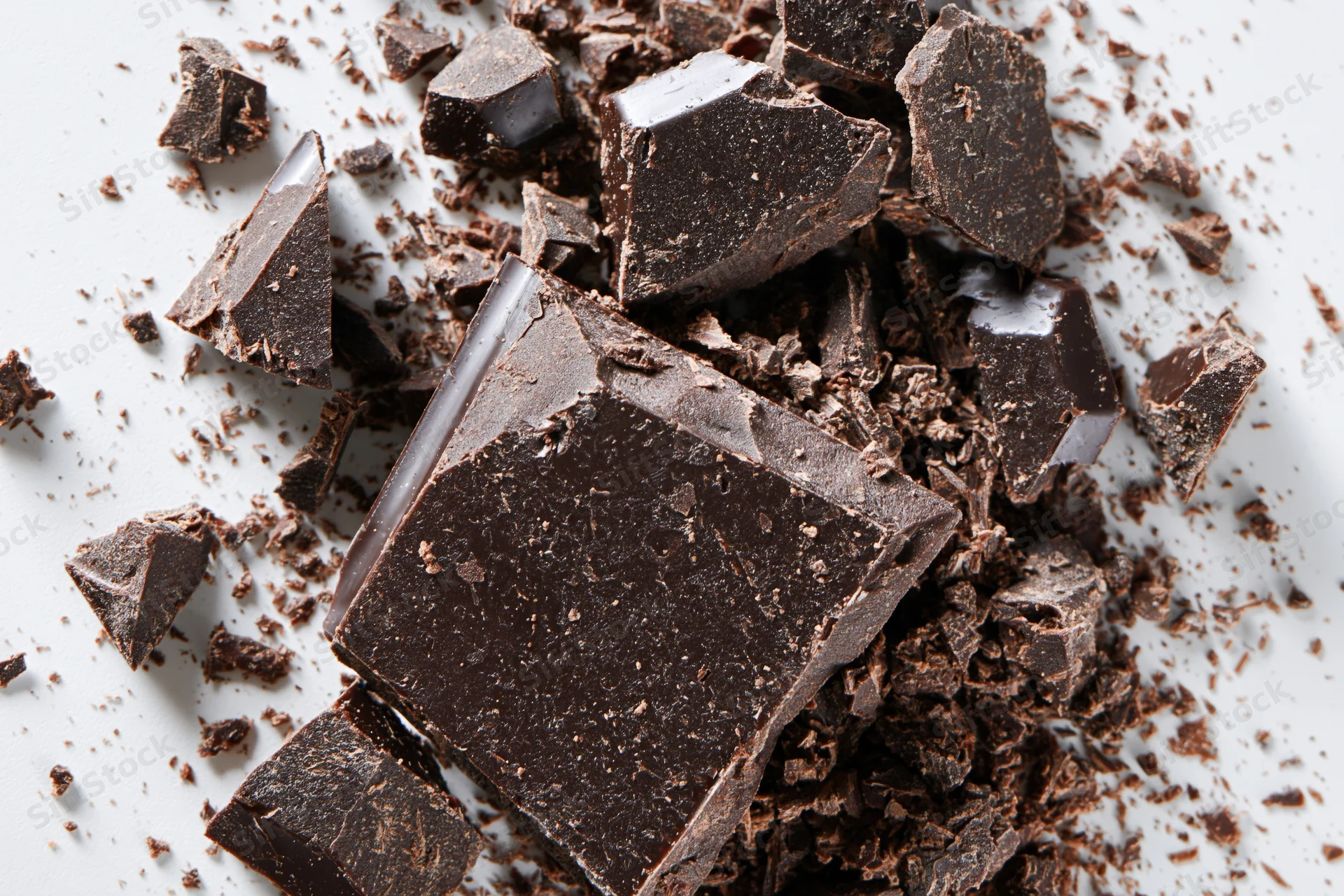 Broken dark chocolate pieces and fine crumbs scattered across a white surface