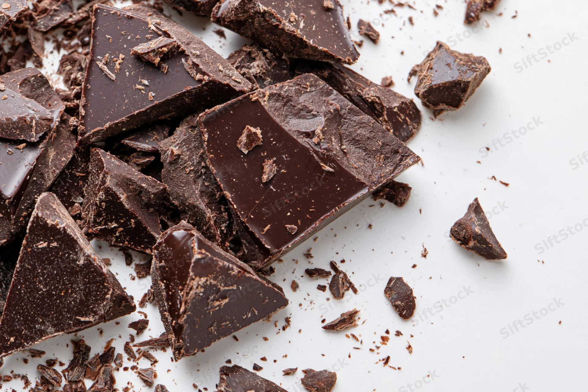 Broken dark chocolate pieces and crumbs scattered on white surface
