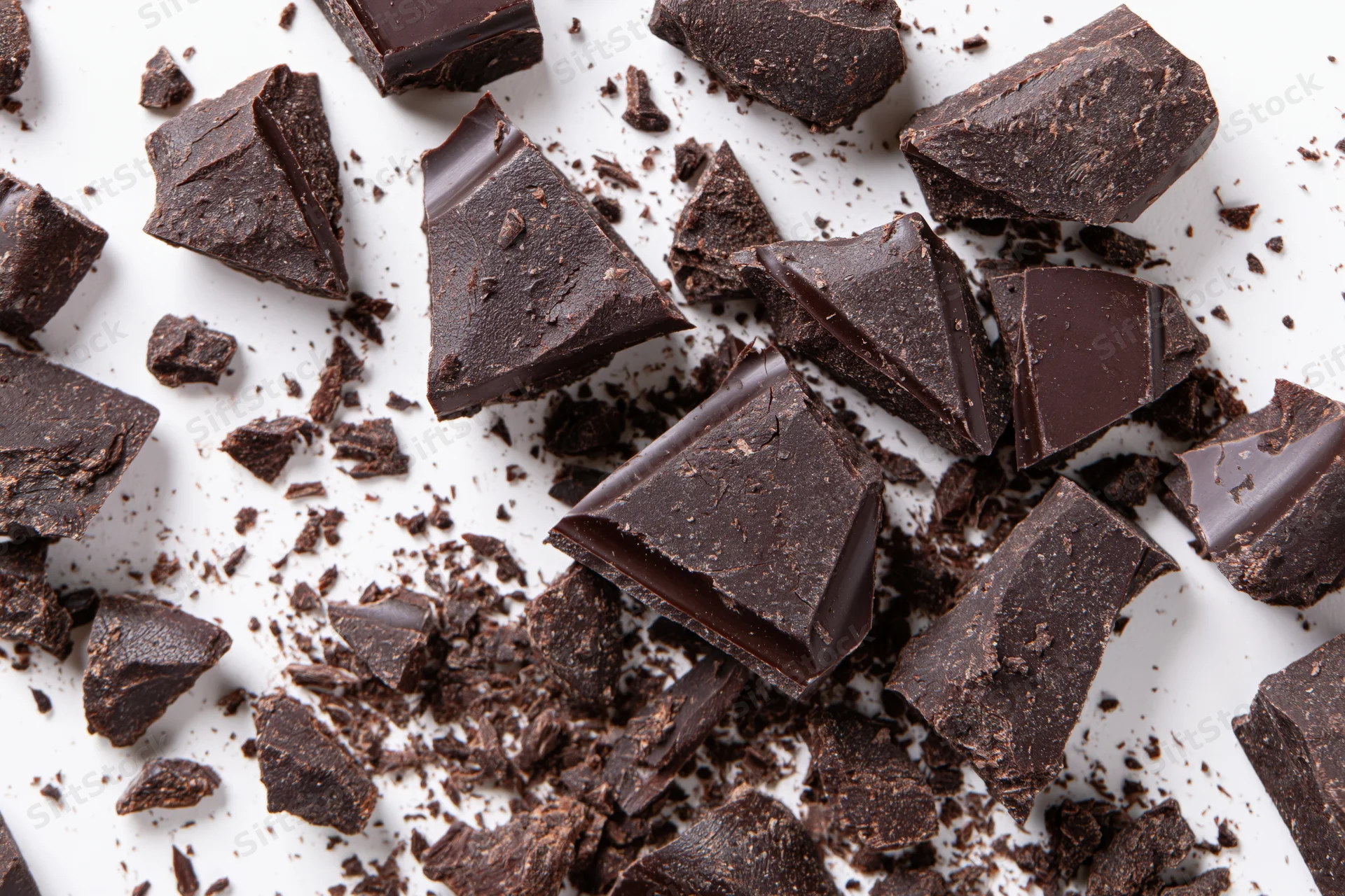 Broken dark chocolate pieces and crumbs scattered across white surface