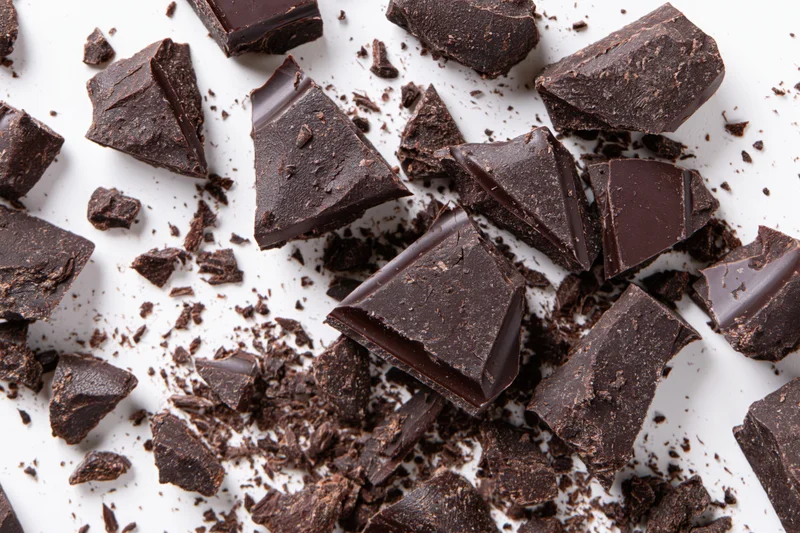 Broken dark chocolate pieces and crumbs scattered across white surface