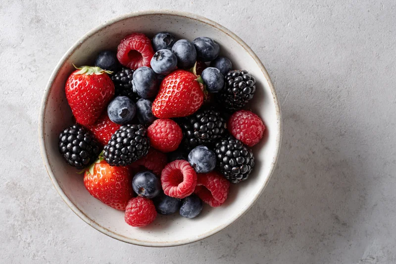 Mixed berries in a ceramic bowl on a light stone surface