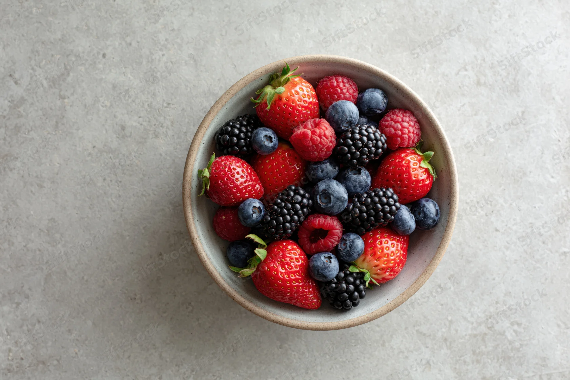 Ceramic bowl filled with fresh mixed berries on gray countertop, overhead view