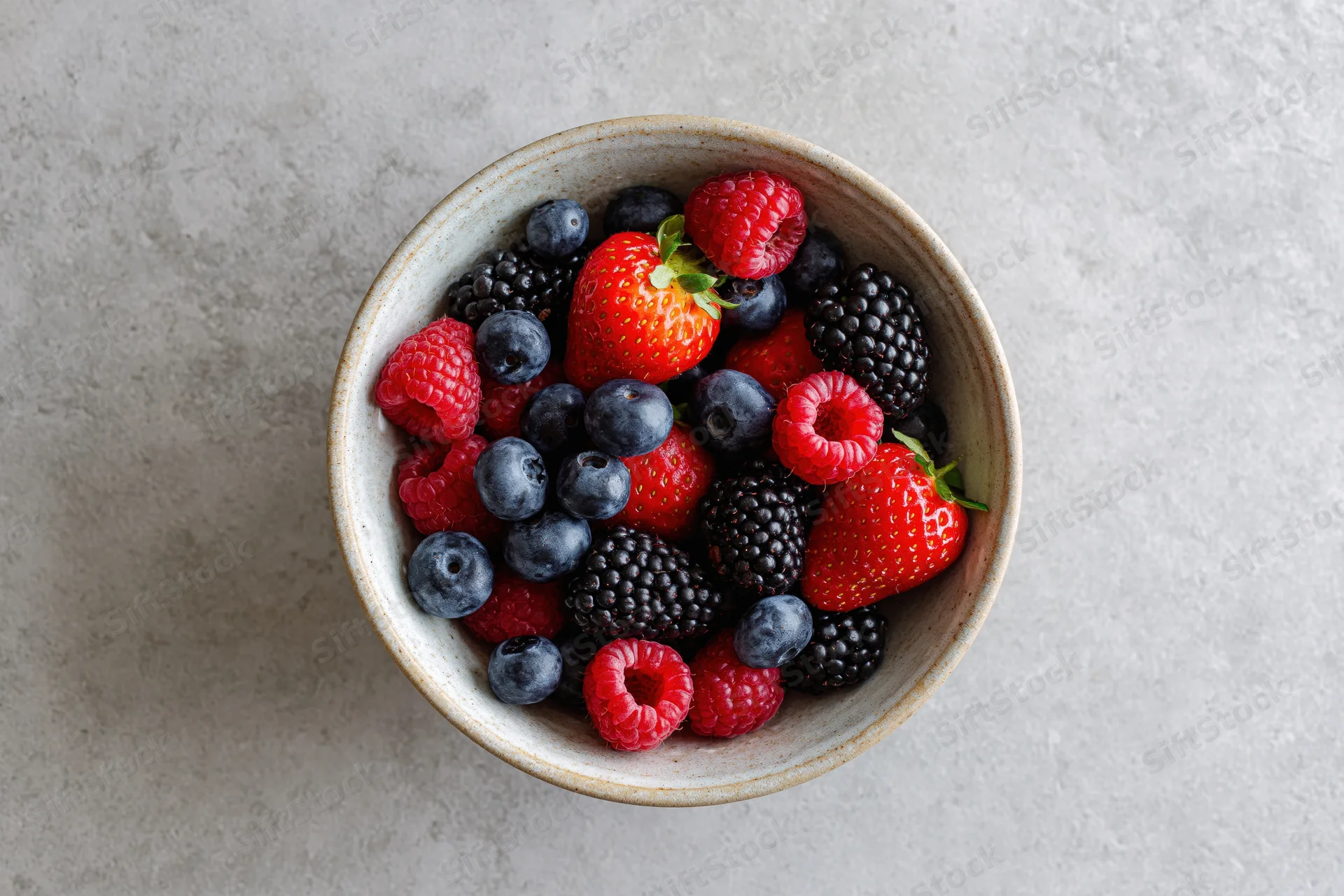 Ceramic bowl filled with mixed fresh berries on a gray countertop, top view
